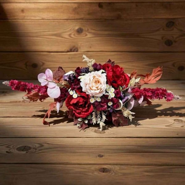 A romantic bouquet of red and blush flowers with white daisies on a wooden floor, accented with dried stems in warm tones.