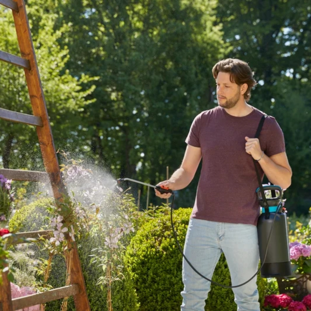 Tlakovy postrekovač gardena 5l comfort strana s odmerkou použitie v záhrade | záhradníctvo garden team Záhradný postrekovač gardena comfort 5l zavesený na pleci záhradkára ktorý ním ošetruje rastliny