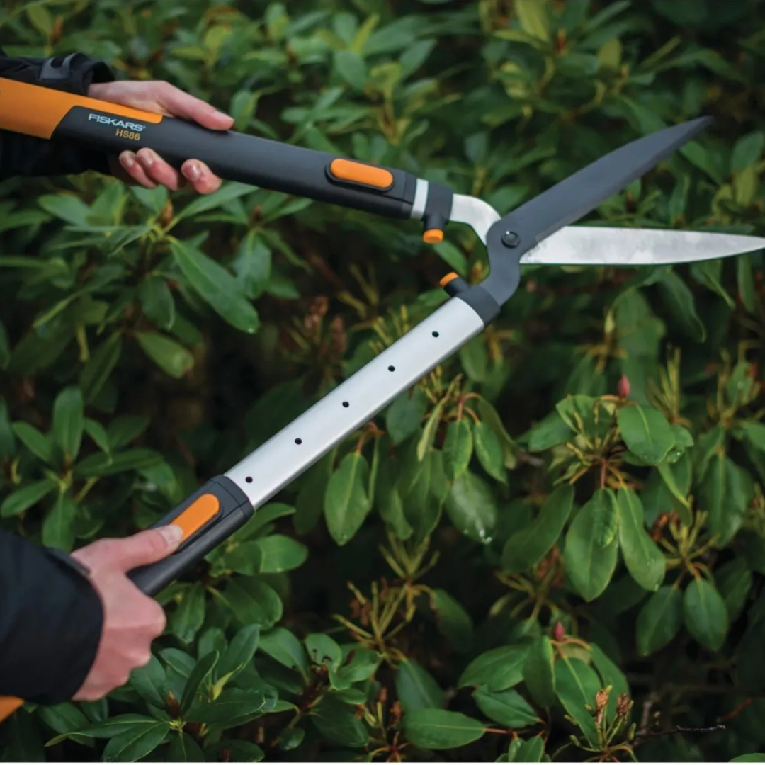 Nožnice na živý plot fiskars hs86 smartfit teleskopické 03 | záhradníctvo garden team Person using a long handled hedge trimmer to prune dense shrubs outdoors