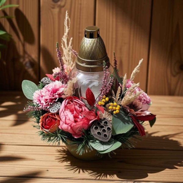 Floral centerpiece with a glass lantern and gold lid, pink peonies, red roses, and dried grasses on a wooden table.